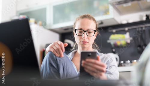 Stay at home and social distancing. Woman in her casual home clothing working remotly from kitchen dining table. Video chatting using social media with friend, family, business clients or partners. photo