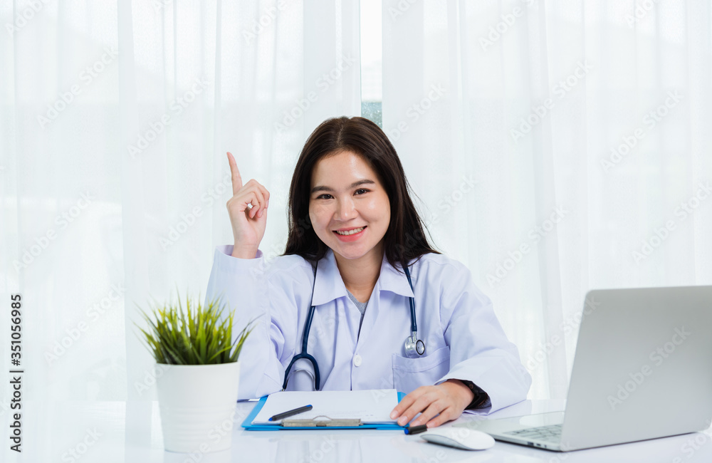 Asian doctor young beautiful woman smiling using working with laptop computer and her writing something on clipboard white paper and point finger up at hospital desk office, Healthcare medical concept Asian doctor young beautiful woman smiling using working with laptop computer and her writing something on clipboard white paper and point finger up at hospital desk office, Healthcare medical concept