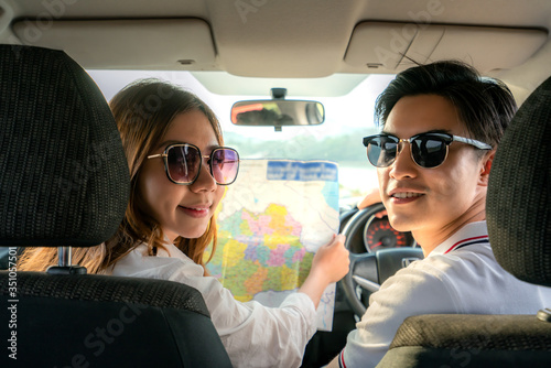 Back view of Young asian couple with woman using a map on a road trip for directions and man driving sitting in a car. Travel concept. © ake1150
