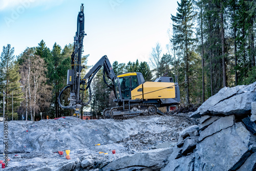 Foto Side view at yellow drilling machine which stands on granite rock and boring holes for dynamite at rock blasting area - further rock exploding, new road construction