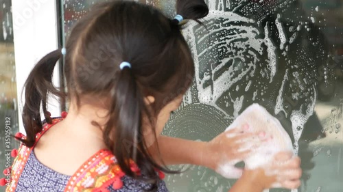 Litttle baby girl's hands holding sponge and cleaning a house sliding door - child's development by letting them do household chores