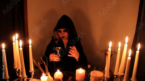 Female Fortuneteller divines in a dark room, candles are burning on a round esoteric table with a pentagram, animal skulls lie, the concept of magic, witchcraft photo