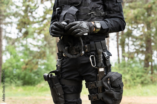 Midsection of unknown man standing in the woods in nature wearing black special forces military or police uniform playing laserwar or lasertag holding smart RGB headband for laser tag