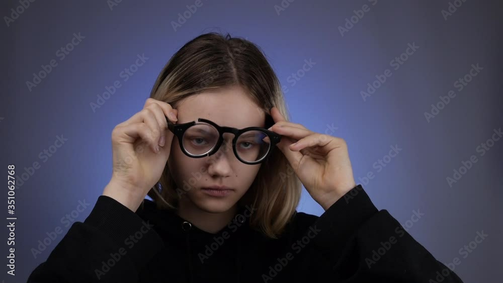 Portrait of a beautiful teenager girl trying to wear broken glasses, and laughs after an unsuccessful attempt. Blue background.Close-up. Portrait of a beautiful teenager girl trying to wear broken glasses, and laughs after an unsuccessful attempt. Blue background.Close-up.