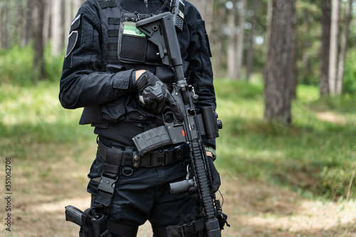 Midsection of unknown man standing in the woods in nature wearing black special forces military or police uniform playing laserwar lasertag airsoft game holding rifle replica infrared sensor laser tag
