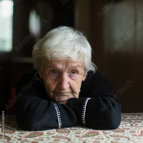 Portrait of a unhappy old woman pensioner sitting at a table.