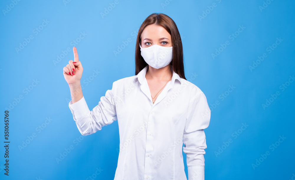 Portrait of an attractive young female doctor in white coat and mask, show one finger Portrait of an attractive young female doctor in white coat and mask, show one finger