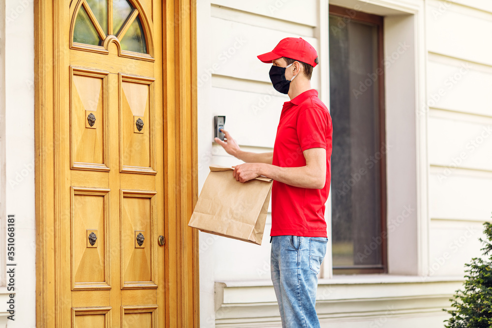 A courier in a protective medical mask delivers takeaway food. Service delivery in terms of quarantine, pandemic coronavirus A courier in a protective medical mask delivers takeaway food. Service delivery in terms of quarantine, pandemic coronavirus