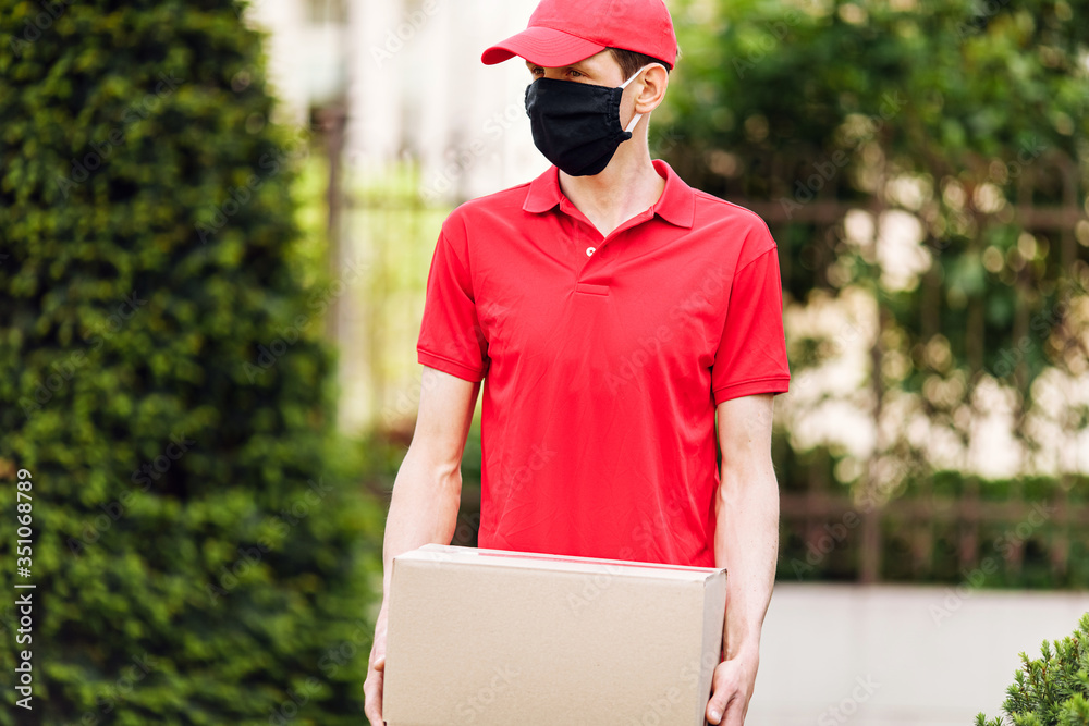The courier holds cardboard boxes in a medical protective mask. Fast and free delivery by transport. The courier holds cardboard boxes in a medical protective mask. Fast and free delivery by transport.