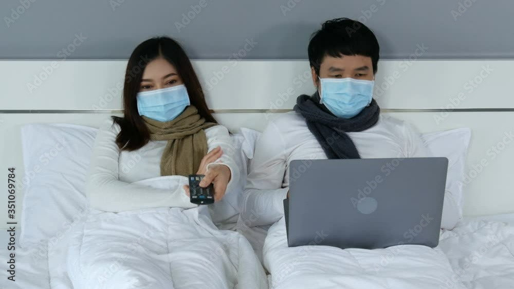 married couple in medical masks watching tv and using laptop on a bed, protection from coronavirus (covid-19) pandemic concept. 4k video married couple in medical masks watching tv and using laptop on a bed, protection from coronavirus (covid-19) pandemic concept. 4k video