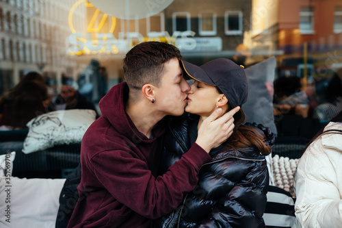 Guy and a girl are kissing at a table in a outdoor cafe.