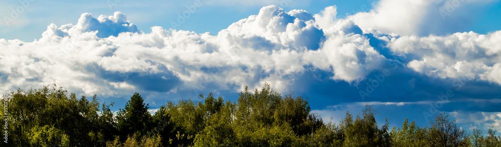 Landscape with fluffy clouds on a blue sky. Banner format for design.