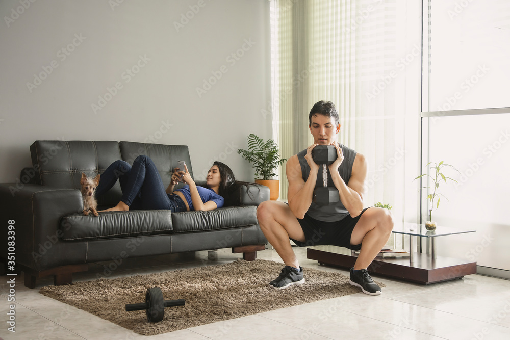 man accompanied by girlfriend with a dog doing dumbbell squat