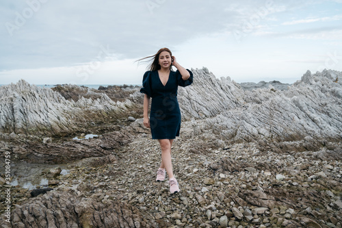 Portrait of young asian woman on stones near sea. Beautiful girl is resting on coast  enjoying outdoor recreation at Kaikoura  New zealand.