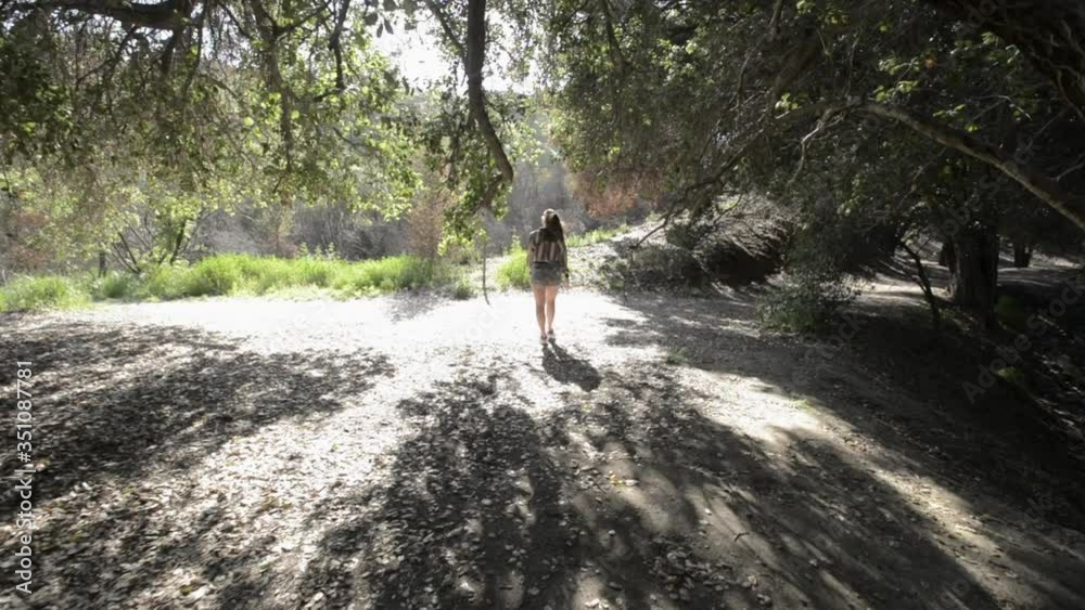 Young woman walking trough the forest trees and going towards the sun light on a sunny day. Young woman walking trough the forest trees and going towards the sun light on a sunny day.