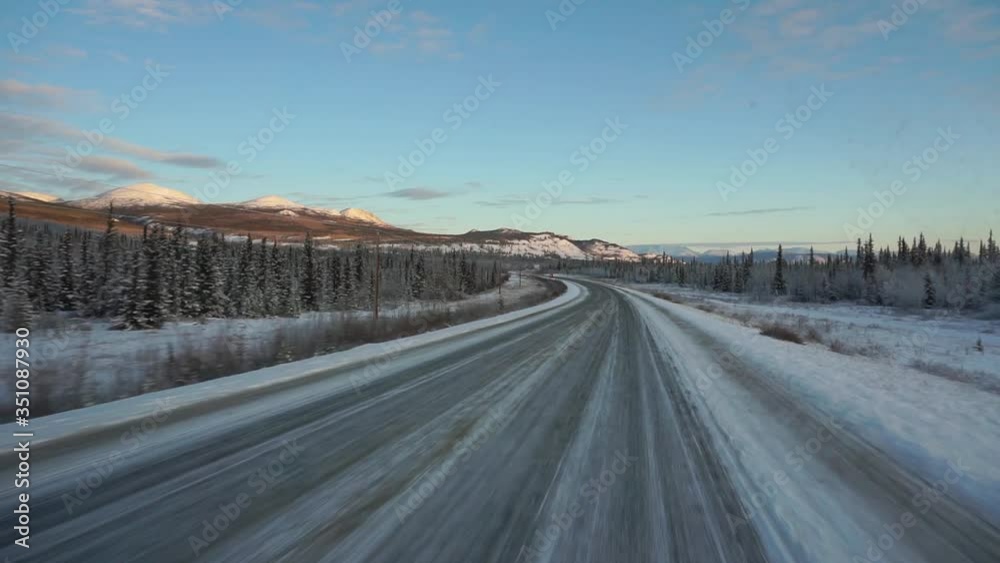 POV view driving on slippery road, in middle of snowy mountains, frosty forest and polar nature, at sunset, in Yukon, Canada POV view driving on slippery road, in middle of snowy mountains, frosty forest and polar nature, at sunset, in Yukon, Canada