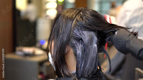 Applying cream hair conditioner mask treatment solution on hair with brush  Close-up on hands and head photo