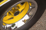 Yellow and chrome wheel of an old timer sports car with black tire reflecting surroundings and photographer