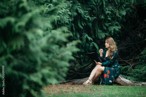 Beautiful asian woman in green dress writing and thinking pose in the park with green leaves.