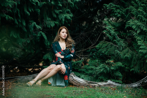 Beautiful asian woman in green dress sit and taking views in the park with green leaves.