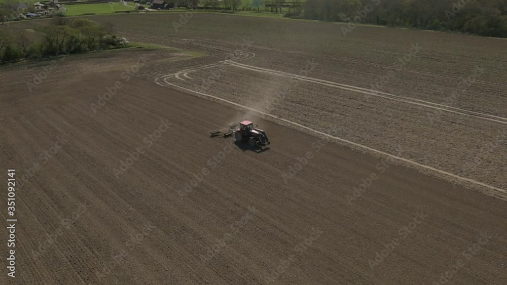 Aerial shot of the tractor ploughing a field in the countryside.