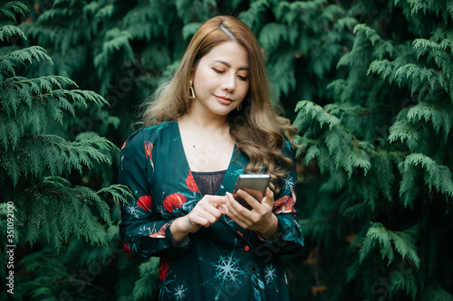 Beautiful asian woman in green dress using cellphone, mibile phone or smartphone pose in the park with green leaves. photo