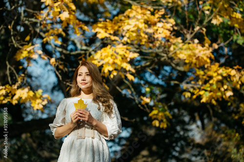Beautiful asian woman with autumn leaves, flower and fall yellow leaves background at Hagley park, Christchruch, New Zealand. photo