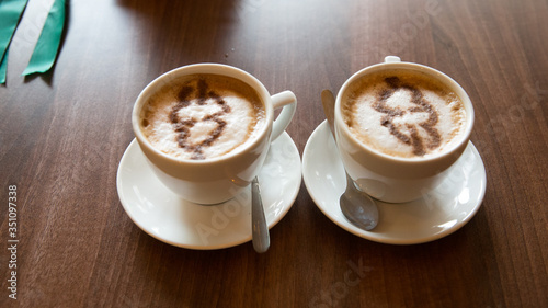 Two cappuccino mugs on which a heart is drawn.