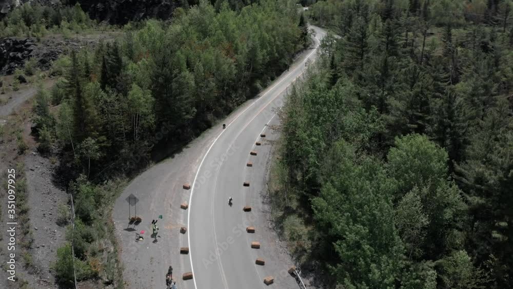 Longboard Racers Moving Fast On The Downhill Of Moutain Road With Few People Watching On The Side At Daytime. - aerial drone shot Longboard Racers Moving Fast On The Downhill Of Moutain Road With Few People Watching On The Side At Daytime. - aerial drone shot