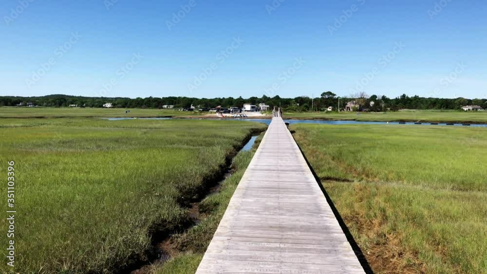 Camera tilt of lonely boardwalk in nature with lush green grass near Town Neck Beach of Sandwich Massachuetts New England USA Camera tilt of lonely boardwalk in nature with lush green grass near Town Neck Beach of Sandwich Massachuetts New England USA