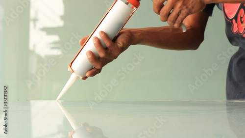 Worker's hands use silicone glue and a glue gun to repair the damaged glass surface.