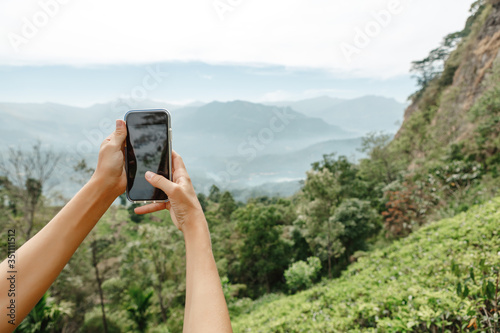 Closeup of  women hands holding mobile phone with wide touchscreen and making photos and video of beautiful nature landscape from high altitude in mountains. Low cloudy sky. Travel and discover © Yevhenii