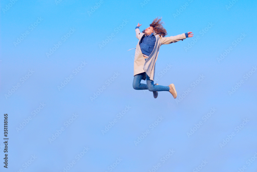 Blurry image of a happy teenage girl jumping up, blue sky background, horizontal view. People, freedom, teens, travel concept.