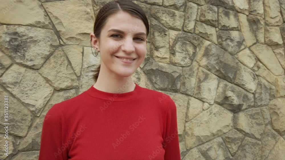 Portrait of cute smiling joyful woman standing by the stone wall. Female enjoying life looking into the camera. Camera moves forward. Portrait of cute smiling joyful woman standing by the stone wall. Female enjoying life looking into the camera. Camera moves forward.