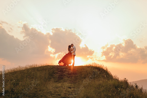 Happy couple stands in embrace and kisses each other on beautiful sunset in mountain.