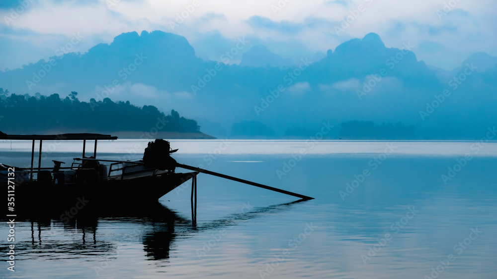 Silhouette view of traditional Thai long tail boat on water lake river with mountain ranges background at “Cheow Lan Dam (Ratchaprapa Dam)” Suratthani Thailand
