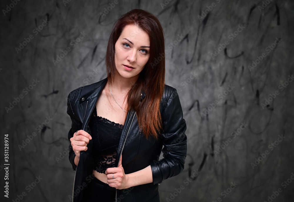 A pretty model is standing on a gray background in a black jacket. Studio portrait of a caucasian brunette girl with minimal makeup. A pretty model is standing on a gray background in a black jacket. Studio portrait of a caucasian brunette girl with minimal makeup.