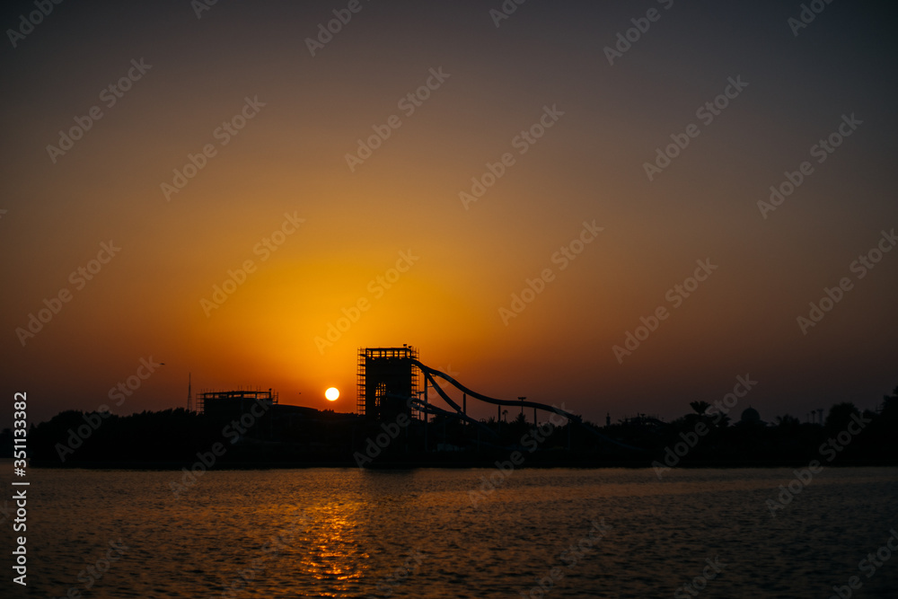 Yellow sunset and the silhouette of a high hill with other attractions of the water Park on the other side of the sea | UNITED ARAB EMIRATES, SHARJAH - 17 OCTOBER 2017.