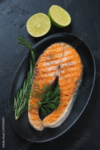 Grilled salmon steak with fresh dill, rosemary and lime served on a black plate, selective focus, vertical shot