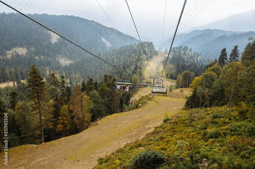 People climb up on a cable car high in the mountains. Green coniferous forest in the mountains in summer.