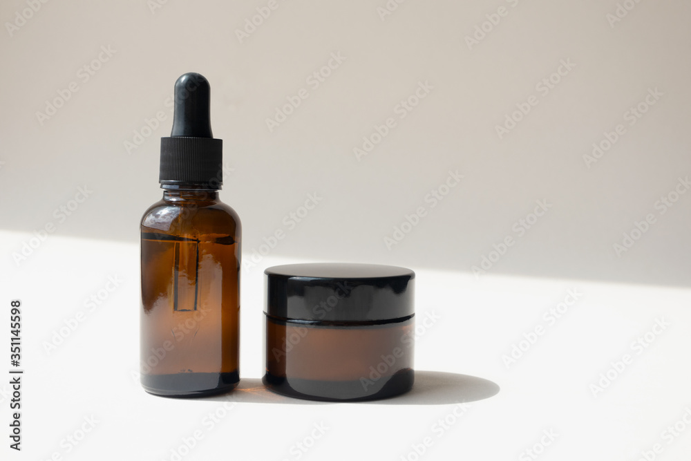 Serum oil essence in brown glass bottle and cream in jar on light beige background with diagonal shadow. Mockup beauty cosmetic products for skincare Serum oil essence in brown glass bottle and cream in jar on light beige background with diagonal shadow. Mockup beauty cosmetic products for skincare