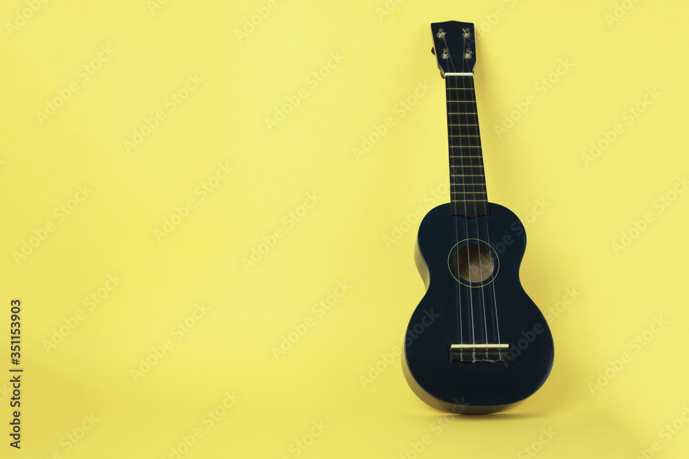 Dark wooden ukulele on yellow background