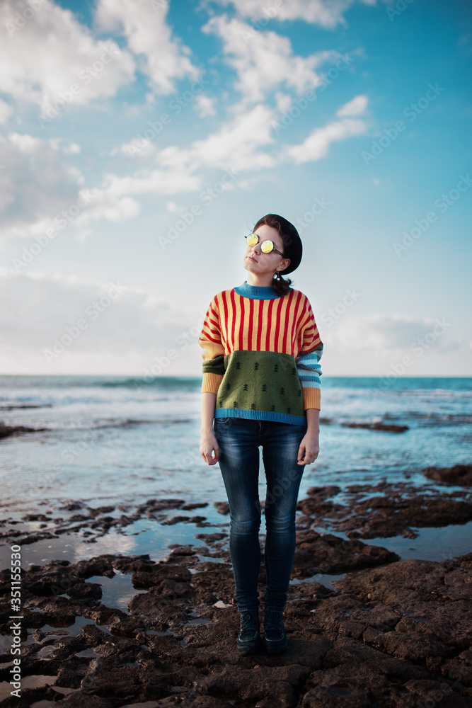 Hipster girl in funny colorful sweater standing at the seacoast