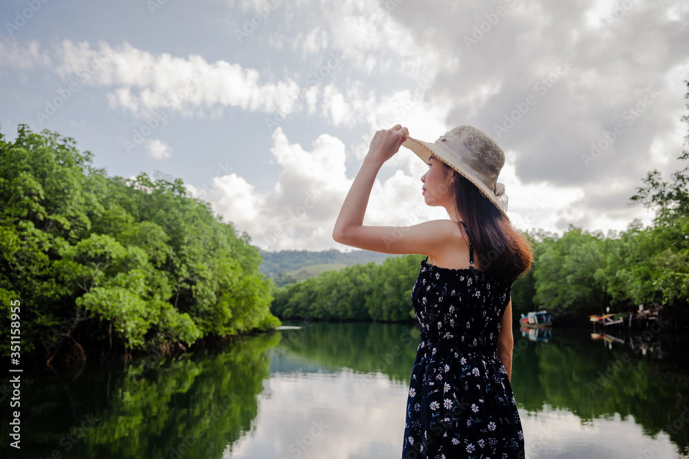 Asian women standing, wearing a hat and admiring the River view with mangrove forest. And the clear skies with beautiful clouds. Suitable for tourism, recreation and relax