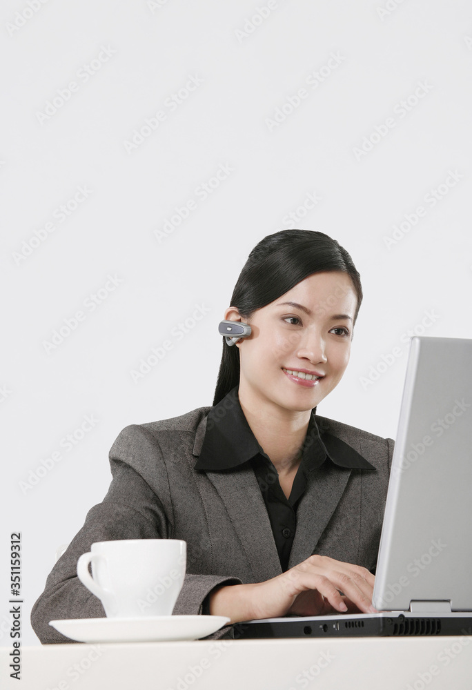 Businesswoman with wireless earpiece using laptop Businesswoman with wireless earpiece using laptop