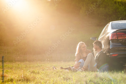 Beautiful young couple having fun at sunset near car