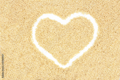 Texture of brown long rice in an even layer. Laid out the outline of a white heart.
