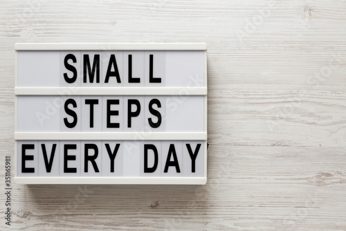 'Small steps every day' words on a lightbox on a white wooden background, top view. Overhead, from above, flat lay. Copy space.