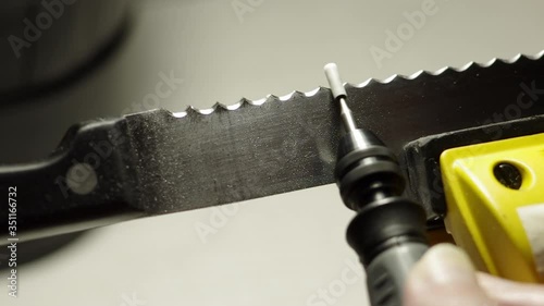 Professional serrated knife blade sharpening with a rotary tool by a manual labour. Macro shot