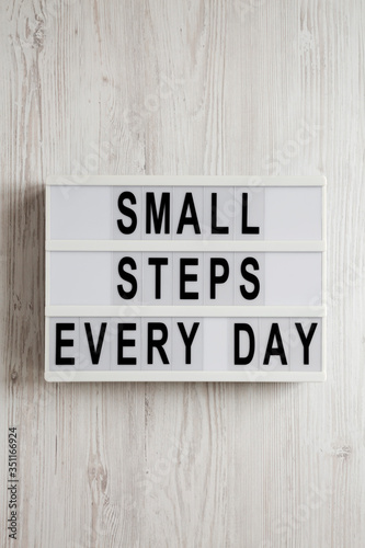 'Small steps every day' words on a lightbox on a white wooden surface, top view. Overhead, from above, flat lay.